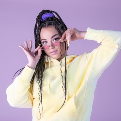 Mulher jovem com hoodie amarelo e óculos de sol contra fundo lilás