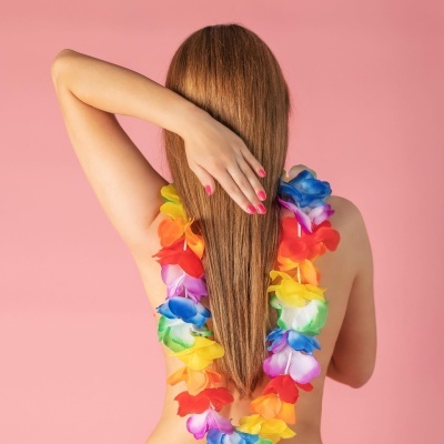 Pessoa de costas com colar de flores coloridas sobre fundo rosa.