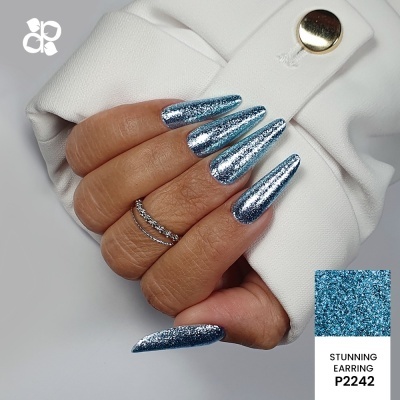 Mão com unhas azuis brilhantes e anéis segurando roupa branca com botão prateado