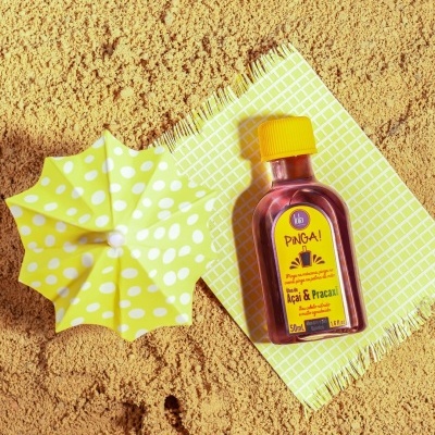 Frasco Pinga! Açaí e Pracaxi com tampa amarela em toalha quadriculada amarela e guarda-sol amarelo na areia