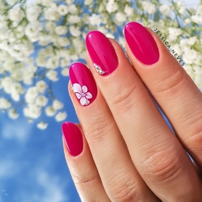 Unhas pintadas em rosa vibrante com decoração floral branca e detalhes prateados