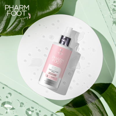 Frasco rosa e branco de produto PHARM FOOT sobre prato branco com gotas de água e folhas verdes