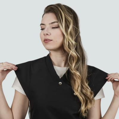 Mulher de cabelo loiro ondulado a usar colete preto com ombreiras e camisola branca por baixo