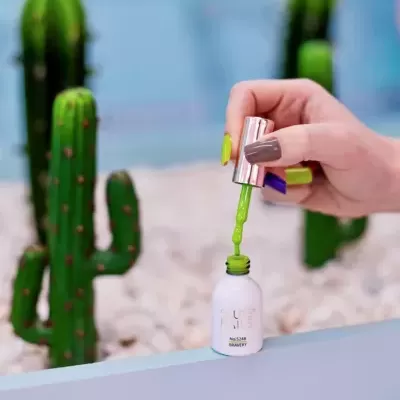 Mão a abrir frasco de verniz verde com cactos ao fundo