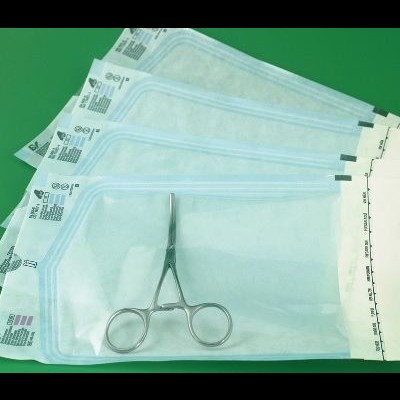 Embalagens transparentes com tesoura cirúrgica metálica sobre fundo verde