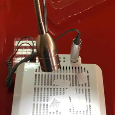 Equipamento elétrico branco com braço metálico flexível em cima de superfície vermelha