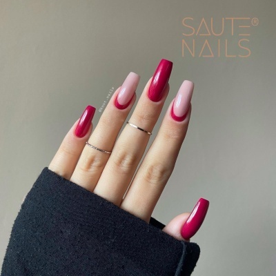Mão feminina com unhas longas em rosa e vermelho com design meia-lua e anéis finos