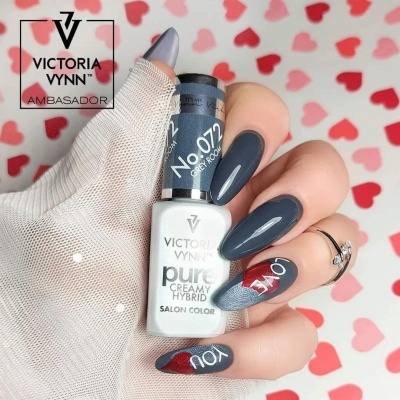 Mão com unhas pintadas de cinza escuro segurando frasco de verniz Victoria Vynn com fundo de corações vermelhos.