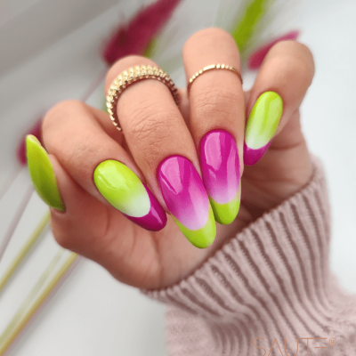 Mão com unhas decoradas em degradê rosa e verde com anéis dourados