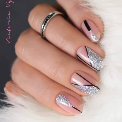 Unhas decoradas com verniz nude, glitter prateado e linhas pretas finas, mão com anel prateado