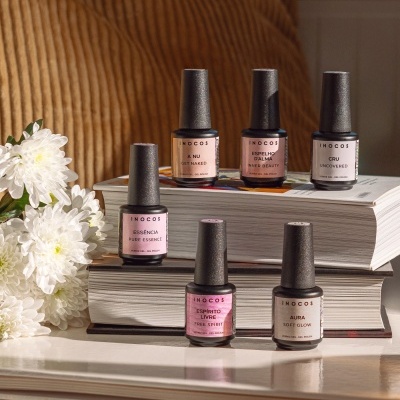 Seis vernizes de unha INOCOS em vários tons sobre livros com flores brancas ao lado