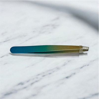 Pinça metálica em gradiente azul para verde-amarelo com ponta inclinada numa superfície marmoreada branca.