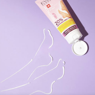 Tubo de creme para pés aberto sobre superfície lilás com creme formando contorno de pé