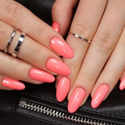 Mãos com unhas cor de coral e anéis prateados sobre fundo preto com fecho