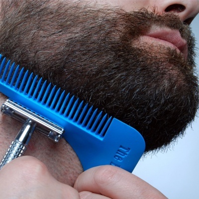 Homem com barba espessa usando pente azul e lâmina de barbear