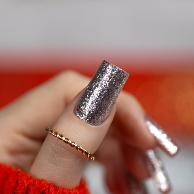 Unhas compridas com esmalte prateado brilhante e anel dourado num fundo desfocado