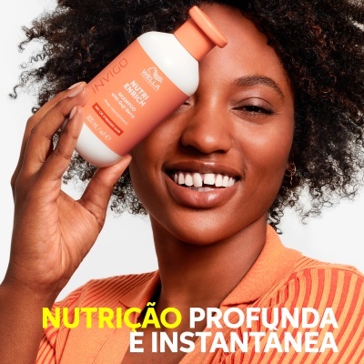 Frasco de produto para cabelo Invigo Nutri-Enrich da Wella Professionals segurado por mulher com cabelo encaracolado.