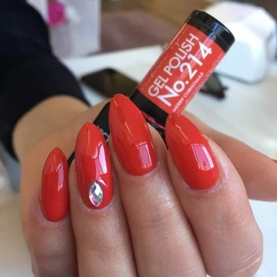 Unhas pintadas com verniz gel vermelho e pedra brilhante num dedo.