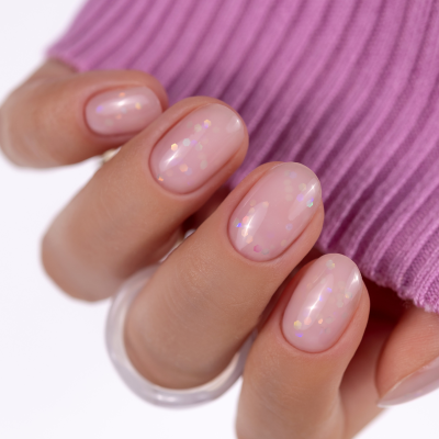Unhas com verniz rosa claro translúcido com brilho holográfico em mão com anel transparente