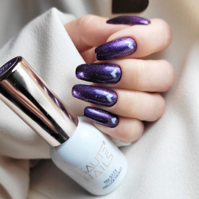 Unhas pintadas de verniz roxo metálico e garrafa branca de verniz com tampa prateada