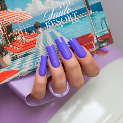 Mão com unhas roxas segurando catálogo de resort com piscina e guarda-sóis