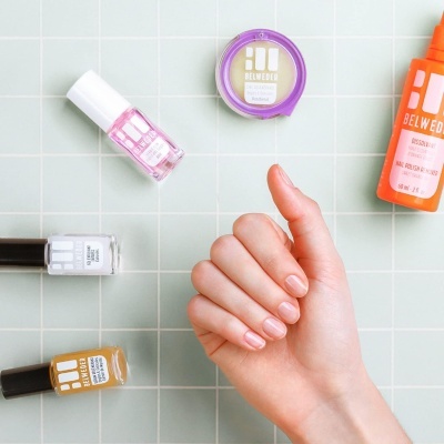 Produtos de manicure BELWEDER sobre azulejos cinzentos com uma mão feminina no centro.