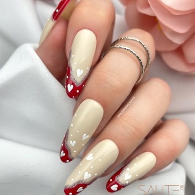 Unhas postiças creme com ponta vermelha e corações brancos decorados, mãos com anéis prateados