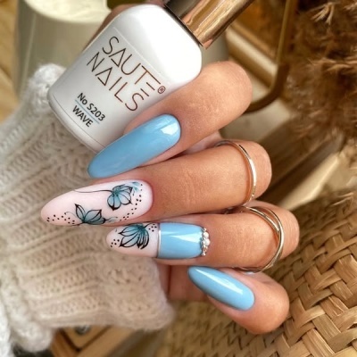 Mãos com unhas azul claro e branca decoradas, segurando verniz SAUTE NAILS