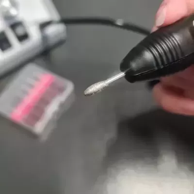 Ponta de ferramenta elétrica preta com acessório prateado e caixa de acessórios ao fundo