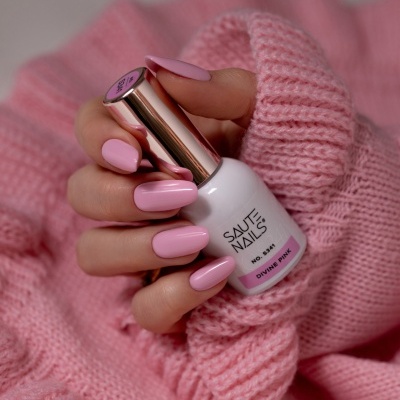Frasco de verniz SAUTE NAILS cor Divine Pink com unhas pintadas da mesma cor em fundo rosa tricotado.