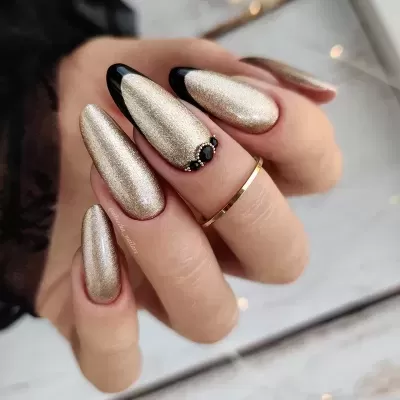 Unhas longas amendoado douradas metálicas com detalhes pretos e pequenos adornos, mão com anel dourado
