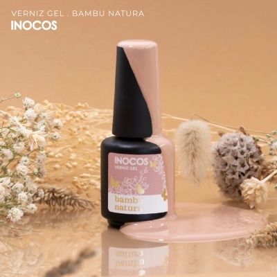 Garrafa de verniz gel rosa INOCOS com verniz derramado e flores secas ao redor