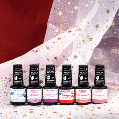 Seis frascos de verniz Inocos coloridos com rótulos em português, sobre superfície branca com estrelas douradas e fundo vermelho com tecido estrelado.