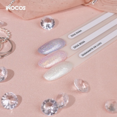 Amostras de verniz de unhas Inocos em tons cintilantes sobre fundo rosa com pedras decorativas.