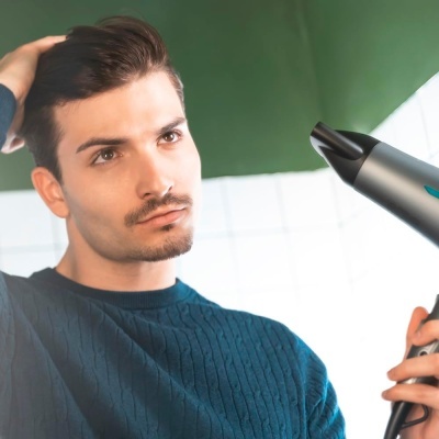Homem jovem a usar secador de cabelo cinzento em ambiente interior