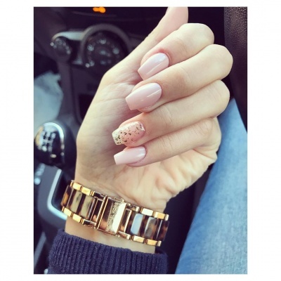 Mão feminina com unhas rosas e relógio dourado dentro de carro