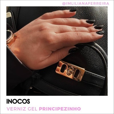 Mão com unhas pretas sobre mala preta com fivela dourada.