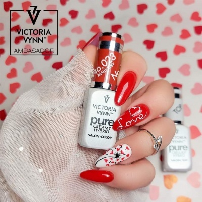 Mãos com unhas vermelhas decoradas com desenho de coração e flores segurando verniz Victoria Vynn.