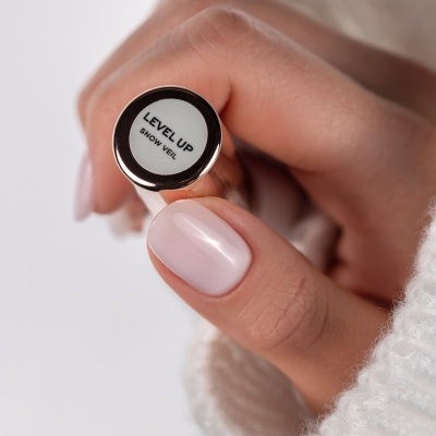 Mão feminina a segurar frasco prateado de verniz para unhas com rótulo LEVEL UP SNOW VEIL