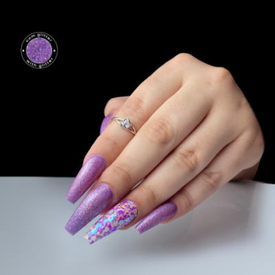 Mão com unhas longas roxas brilhantes e uma decorada com glitter holográfico.