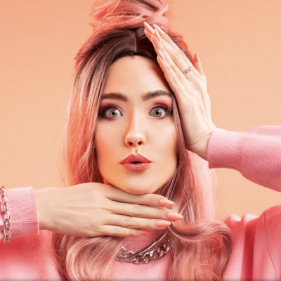 Mulher com cabelo rosa, camisola rosa e fundo pêssego.