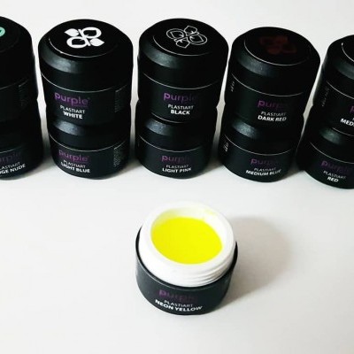 Conjunto de potes de pigmentos coloridos com tampas pretas e símbolos de folhas, um aberto com tinta amarela visível.