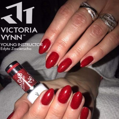 Mãos femininas com unhas vermelhas brilhantes segurando frasco de verniz Victoria Vynn.