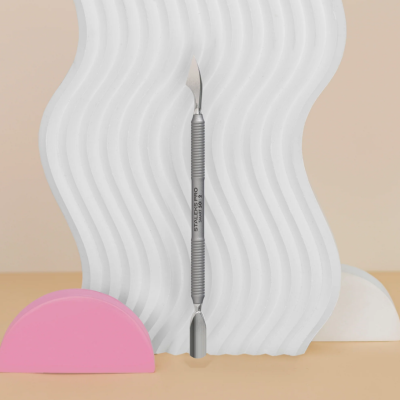 Espátula metálica dupla com inscrição STYLEPRO em fundo bege com decoração branca e rosa