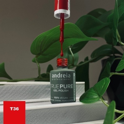 Frasco de verniz gel vermelhos TRUE PURE da andreia professional com pincel e folhas verdes ao fundo