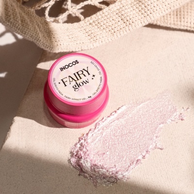 Frasco rosa de gel Inocos Fairy Glow com creme esbranquiçado e brilhante sobre superfície bege