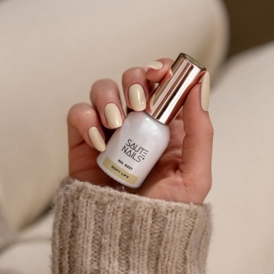 Frasco de verniz de unhas branco com tampa dourada e mão feminina com unhas pintadas de creme