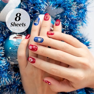 Unhas decoradas com padrões de flocos de neve brancos em vermelho e azul, decoração natalícia azul ao fundo