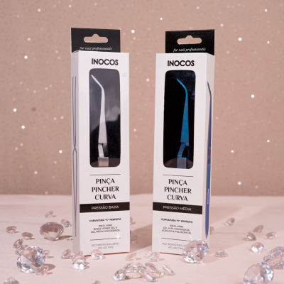 Embalagens brancas de pinças curvadas INOCOS preta e azul sobre fundo bege com cristais transparentes