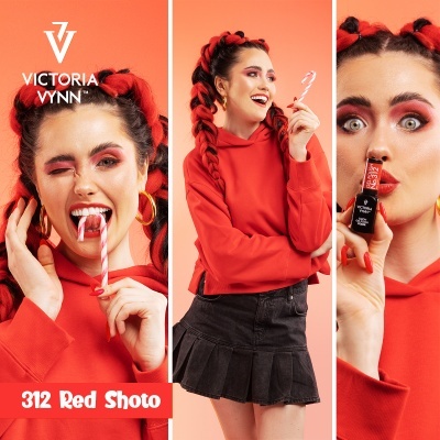 Mulher com hoodie vermelho e saia preta segura bengala doce e batom Victoria Vynn 312 Red Shoto em fundo laranja
